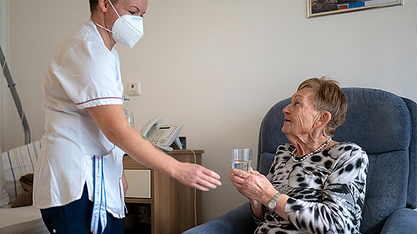 Bild | Pflegerin reicht Seniorin ein Glas Wasser
